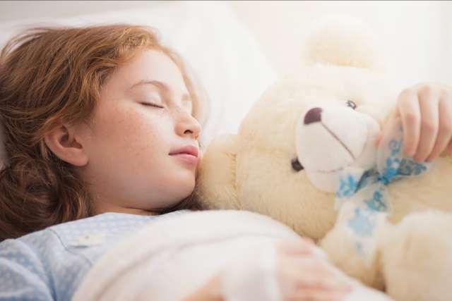 Adorable little girl resting in a hospital bed with her teddy bear.