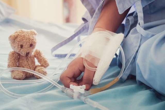 Child's hand and small teddy bear on hospital bed